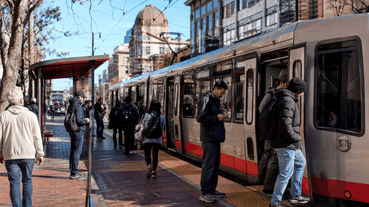 Passengers boarding Muni at a San Francisco stop, with a Muni vehicle at the curb.