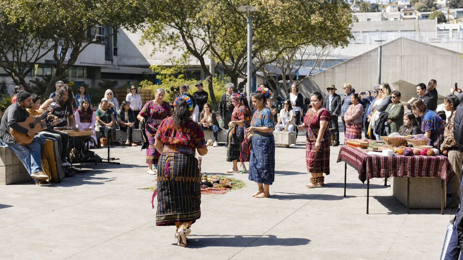 Representative editorial view of a Maya cultural festival in San Francisco with traditional clothing, dance, art tables and families gathered indoors.